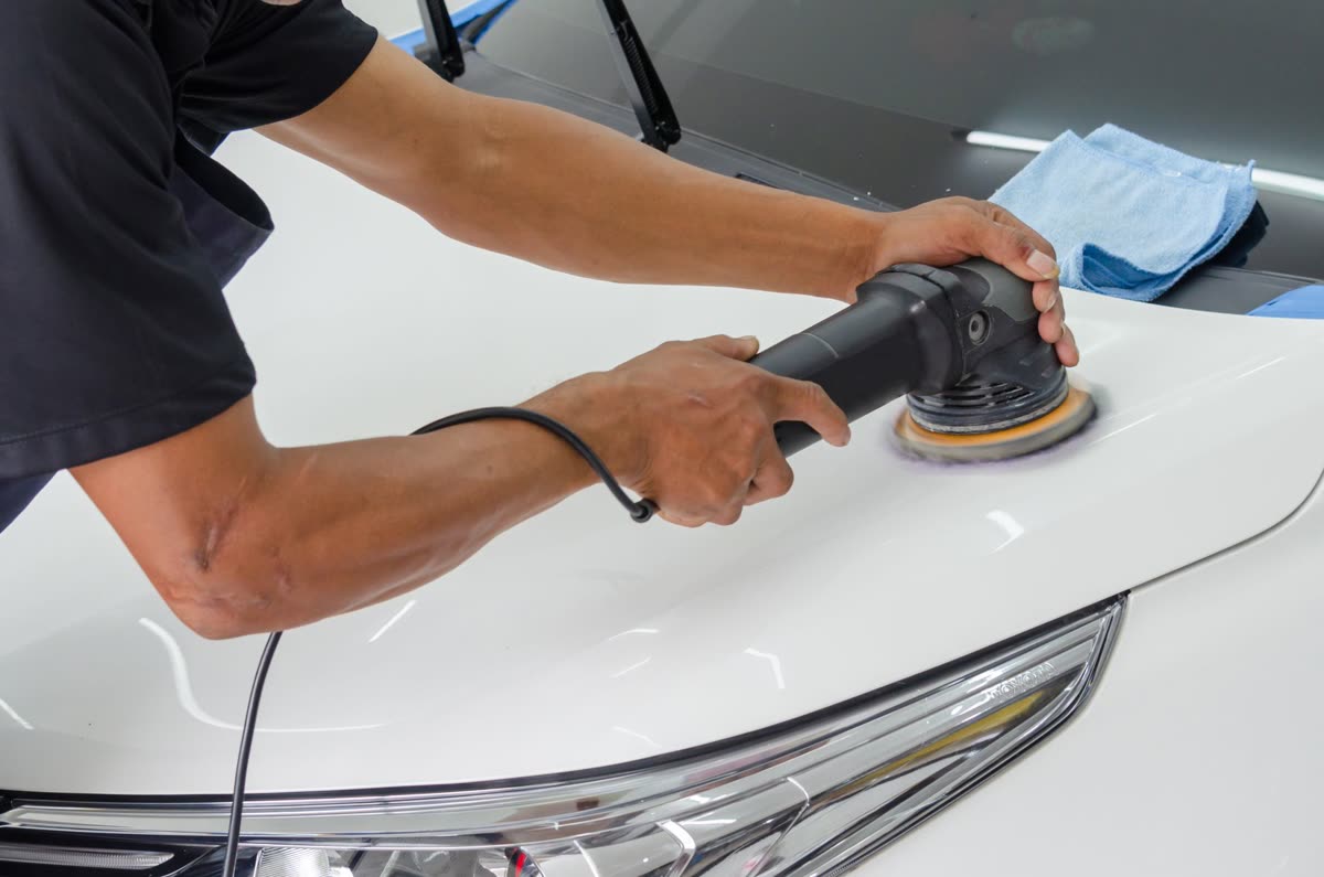 Hands polishing a white car's paintwork with a foam applicator pad